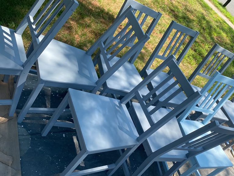 Set of wooden dining chairs freshly painted light blue, drying outdoors on drop cloths