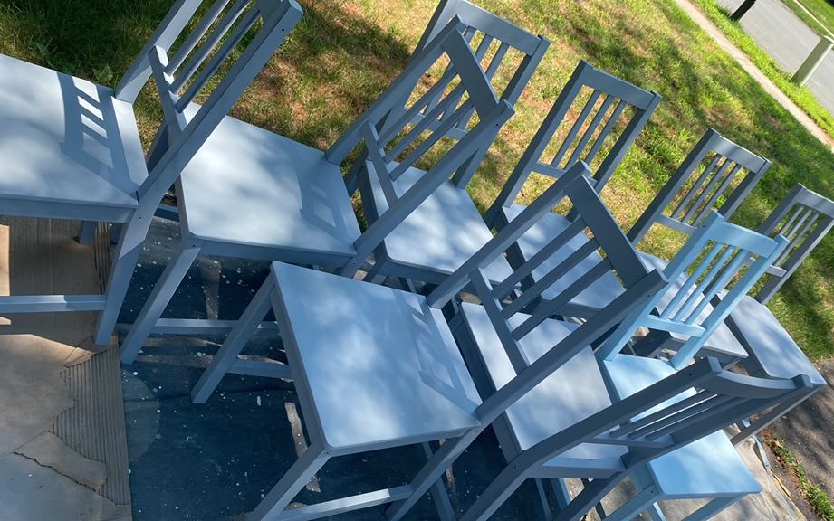 Set of wooden dining chairs freshly painted light blue, drying outdoors on drop cloths