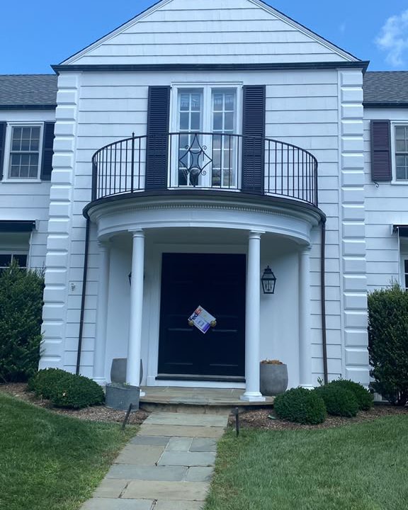 White colonial home with a black front door, columned portico and iron balcony