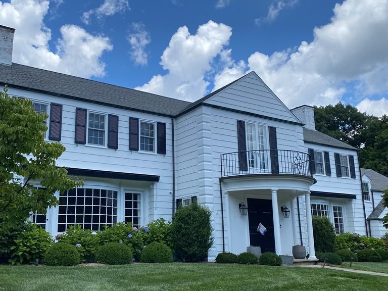 Two-story white colonial with dark shutters, curved portico and landscaped front yard