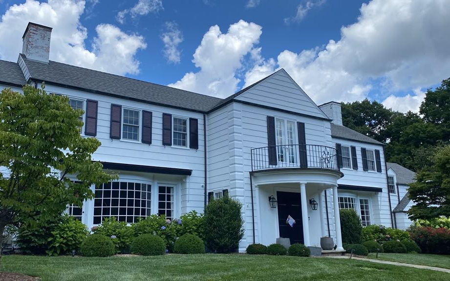 Two-story white colonial with dark shutters, curved portico and landscaped front yard