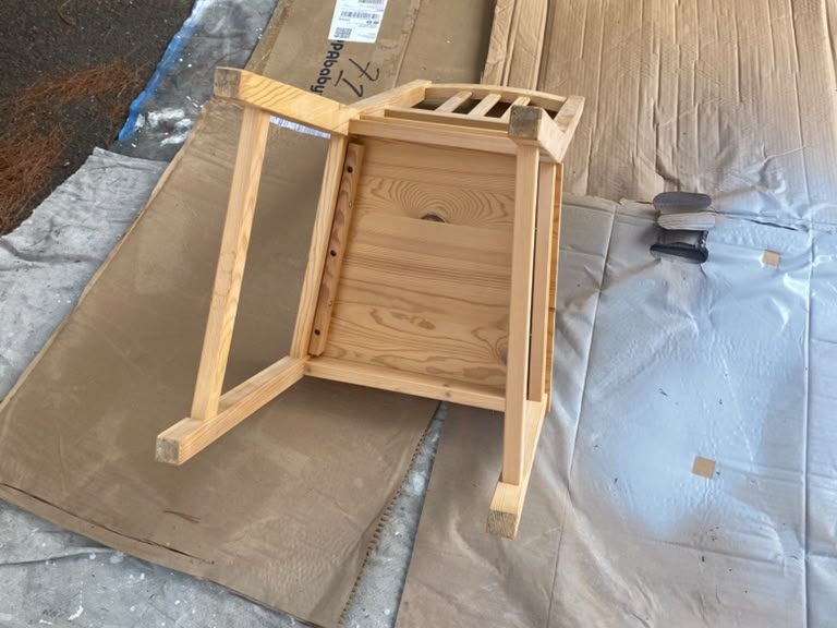Unpainted wooden chair set on cardboard and drop cloths, ready for prep