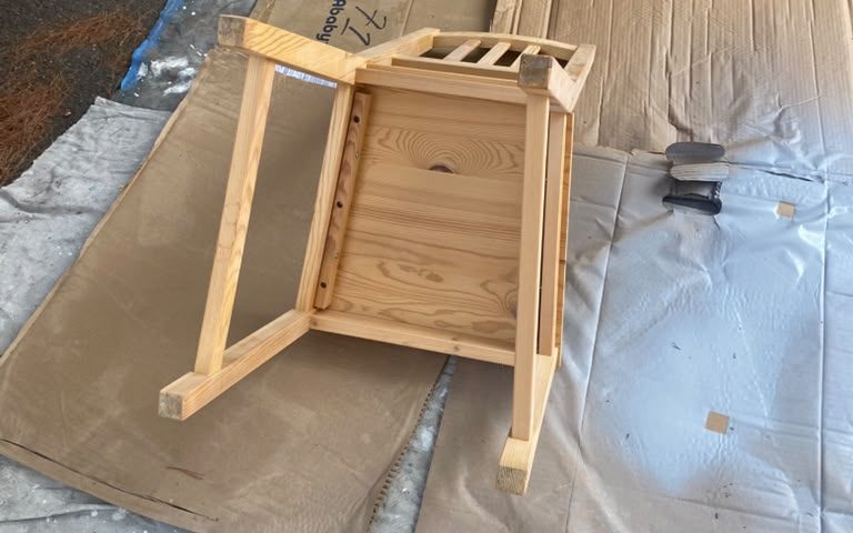 Unpainted wooden chair set on cardboard and drop cloths, ready for prep