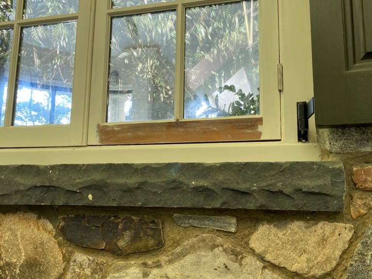 Window above a stone sill with fresh primer on the bottom rail of the sash