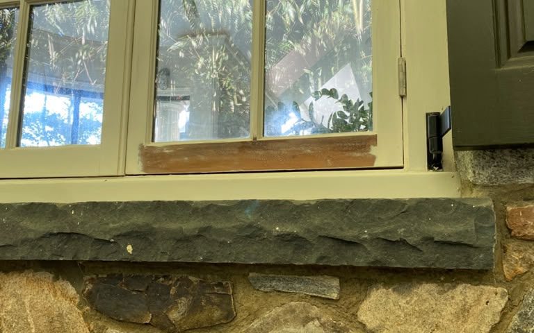 Window above a stone sill with fresh primer on the bottom rail of the sash