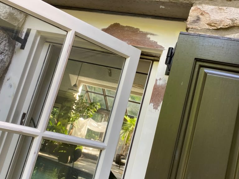 Open casement window and dark green shutter on a stone wall during repainting
