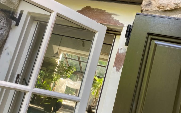 Open casement window and dark green shutter on a stone wall during repainting
