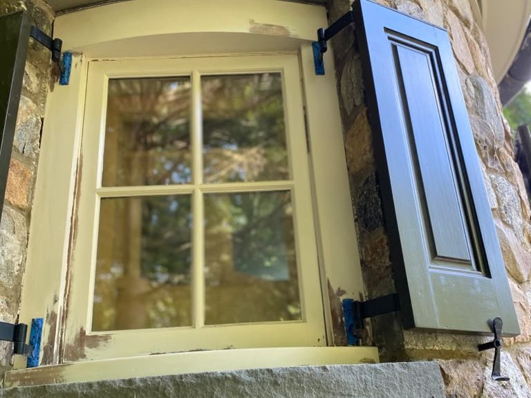 Curved window in a stone tower with dark shutters, before repainting