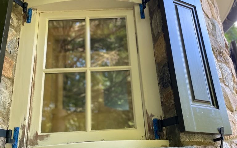 Curved window in a stone tower with dark shutters, before repainting