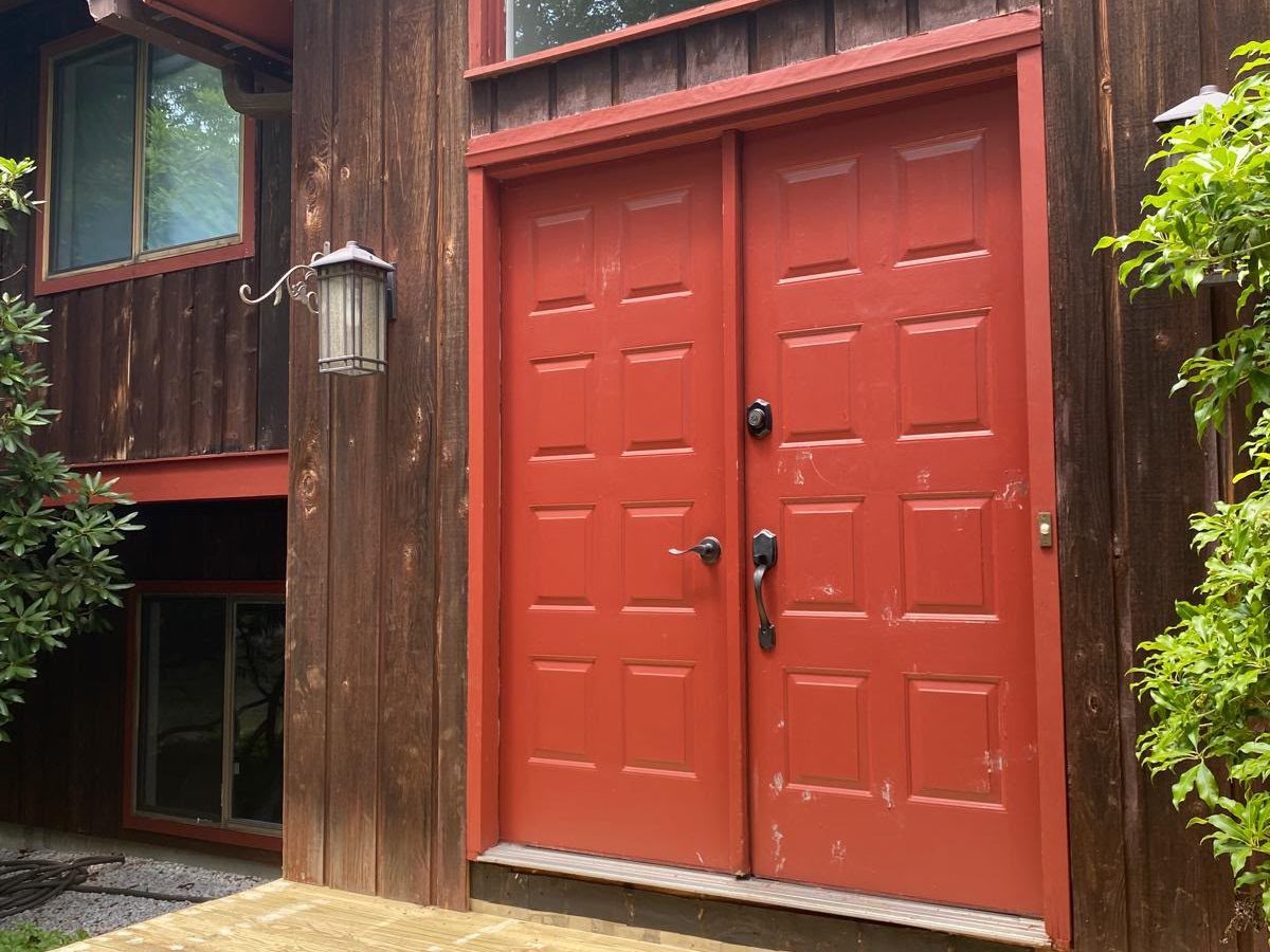 Red double front doors freshly painted, set in dark wood siding above a new deck