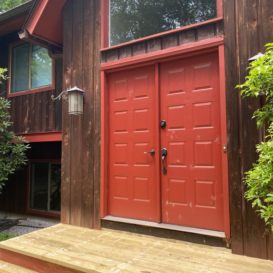 Red double front doors freshly painted, set in dark wood siding above a new deck