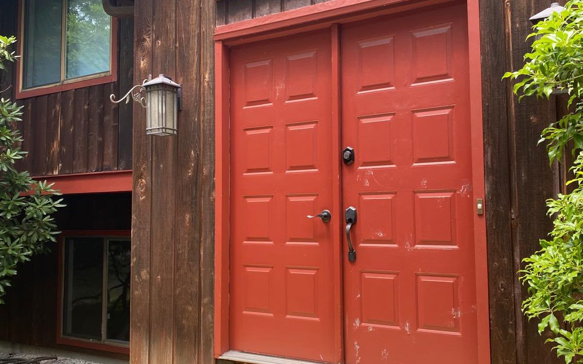 Red double front doors freshly painted, set in dark wood siding above a new deck