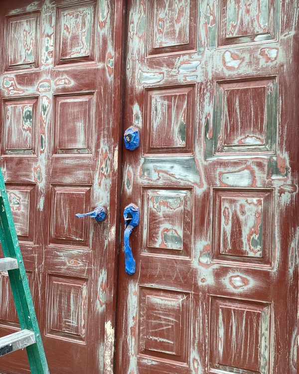 Before: Red double doors sanded and spot-primed, with the hardware masked in blue tape