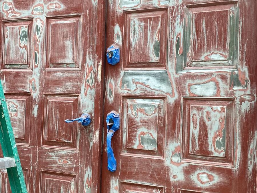 Red double doors sanded and spot-primed, with the hardware masked in blue tape