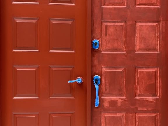 Red double doors mid-project, one leaf painted and the other primed
