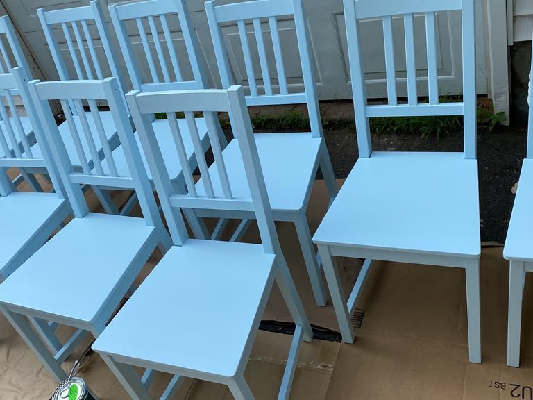 Dining chairs painted light blue, lined up on cardboard outdoors