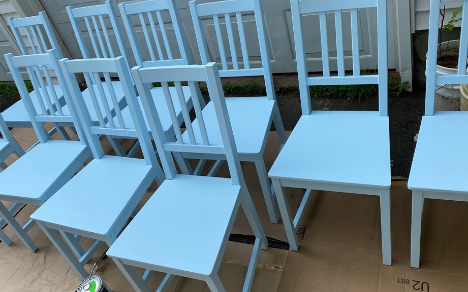 Dining chairs painted light blue, lined up on cardboard outdoors