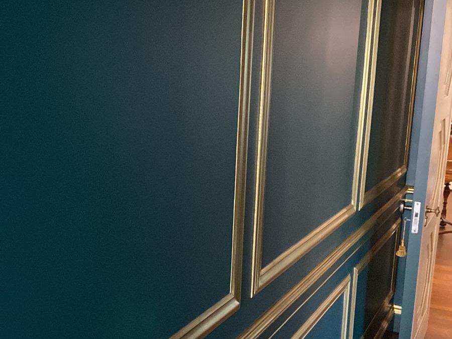 Hallway with deep teal walls and gold-finished picture-frame molding