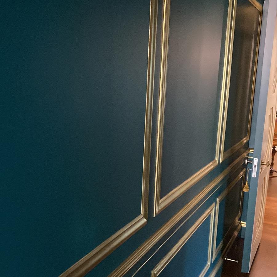 Hallway with deep teal walls and gold-finished picture-frame molding