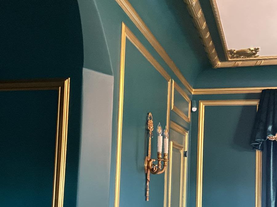 Room with deep teal walls, an arched opening and gilded molding and cornice