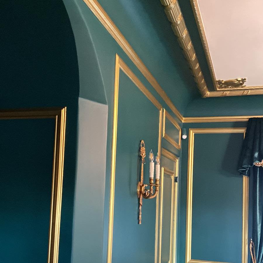Room with deep teal walls, an arched opening and gilded molding and cornice