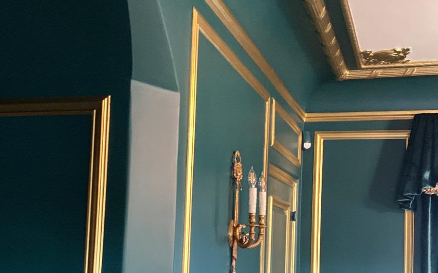 Room with deep teal walls, an arched opening and gilded molding and cornice