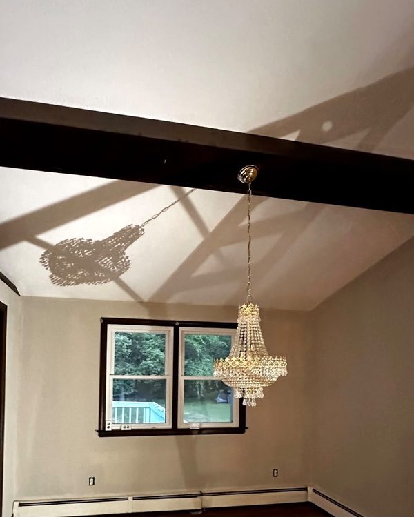 After: Living room with a vaulted white ceiling, dark beams, beige walls and a crystal chandelier