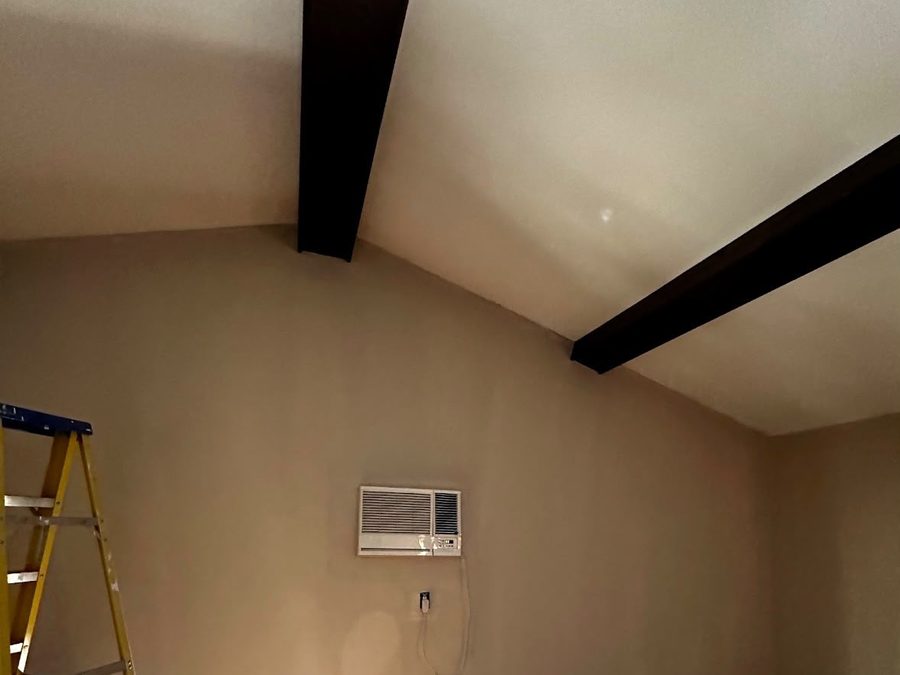 Vaulted room with dark beams and freshly painted walls around a wall air conditioner