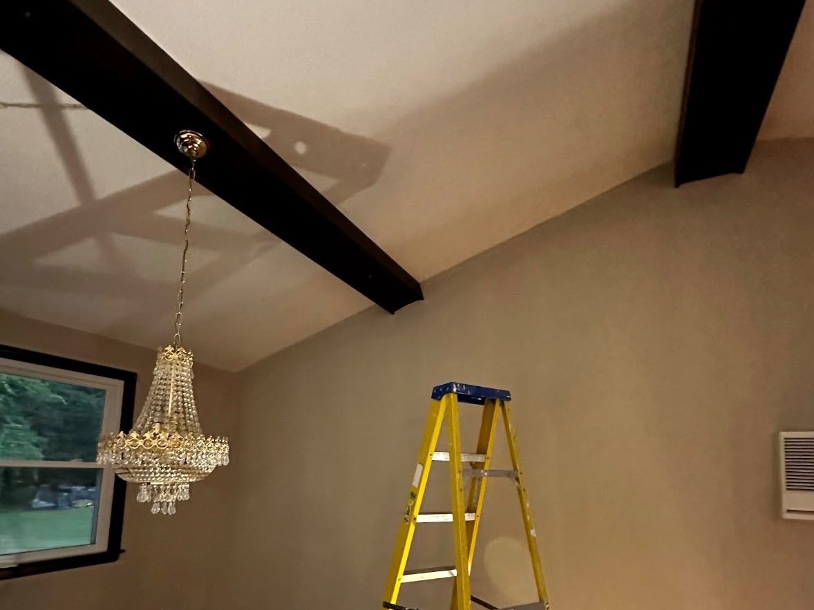 Finished room with dark beams, a white ceiling, a chandelier and a stepladder