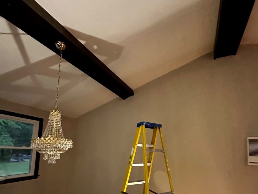 Finished room with dark beams, a white ceiling, a chandelier and a stepladder