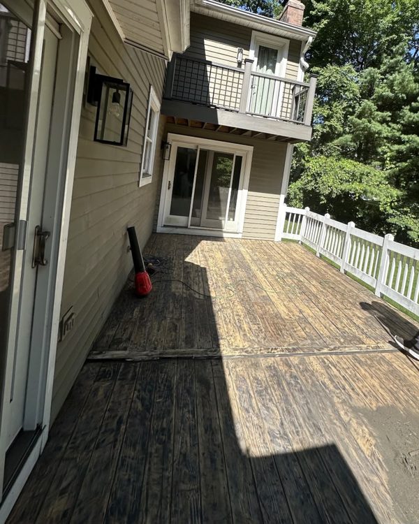 Before: Weathered, stained deck boards beside a two-story house before painting