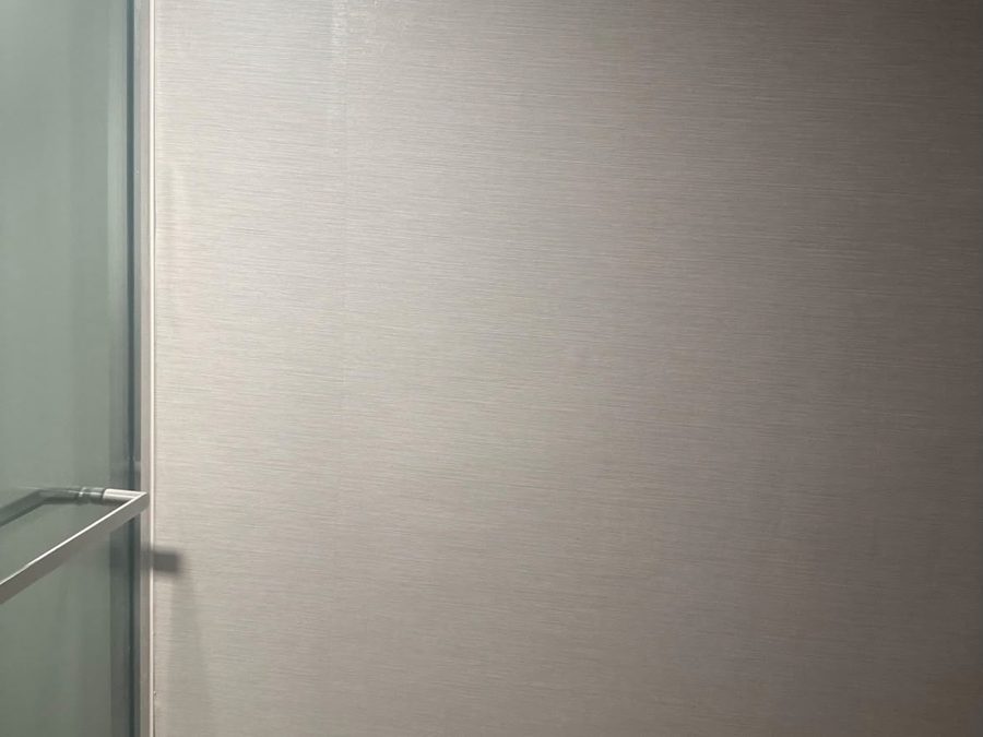 Bathroom wall with a textured gray finish beside a glass shower