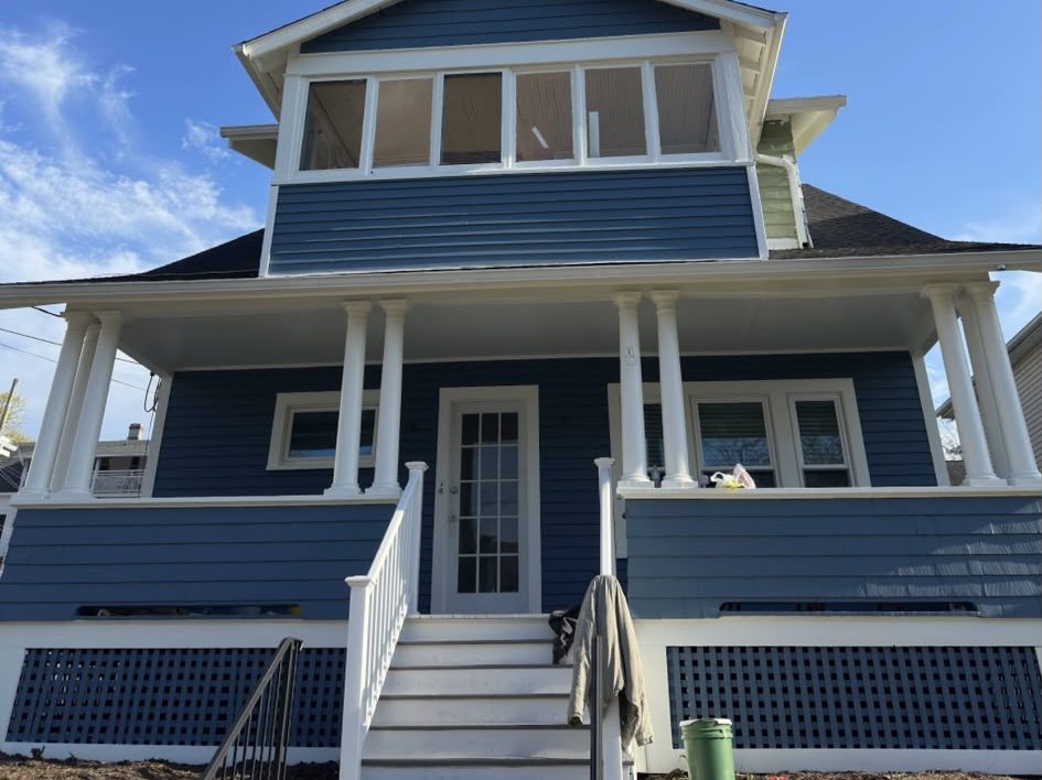 Two-story home painted blue with white columns, railings and lattice