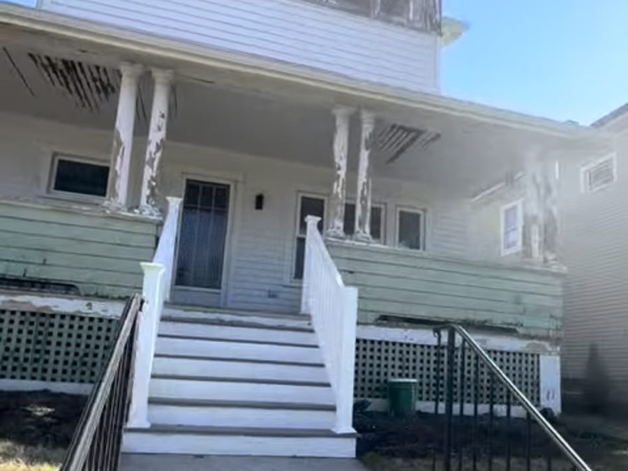 Two-story home with peeling green and white paint on the porch and upper windows