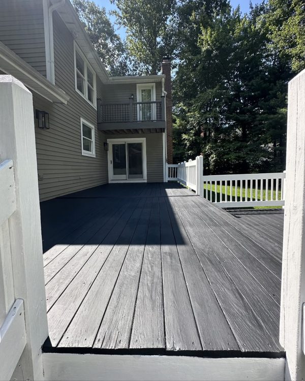 After: Deck boards painted charcoal with white railings beside a two-story house