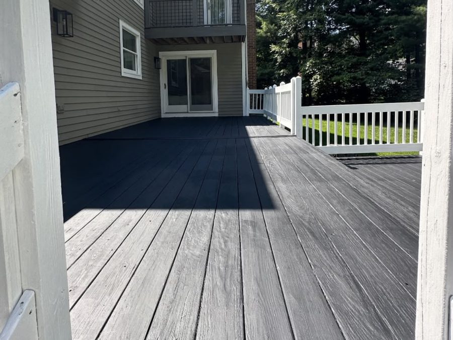 Deck boards painted charcoal with white railings beside a two-story house