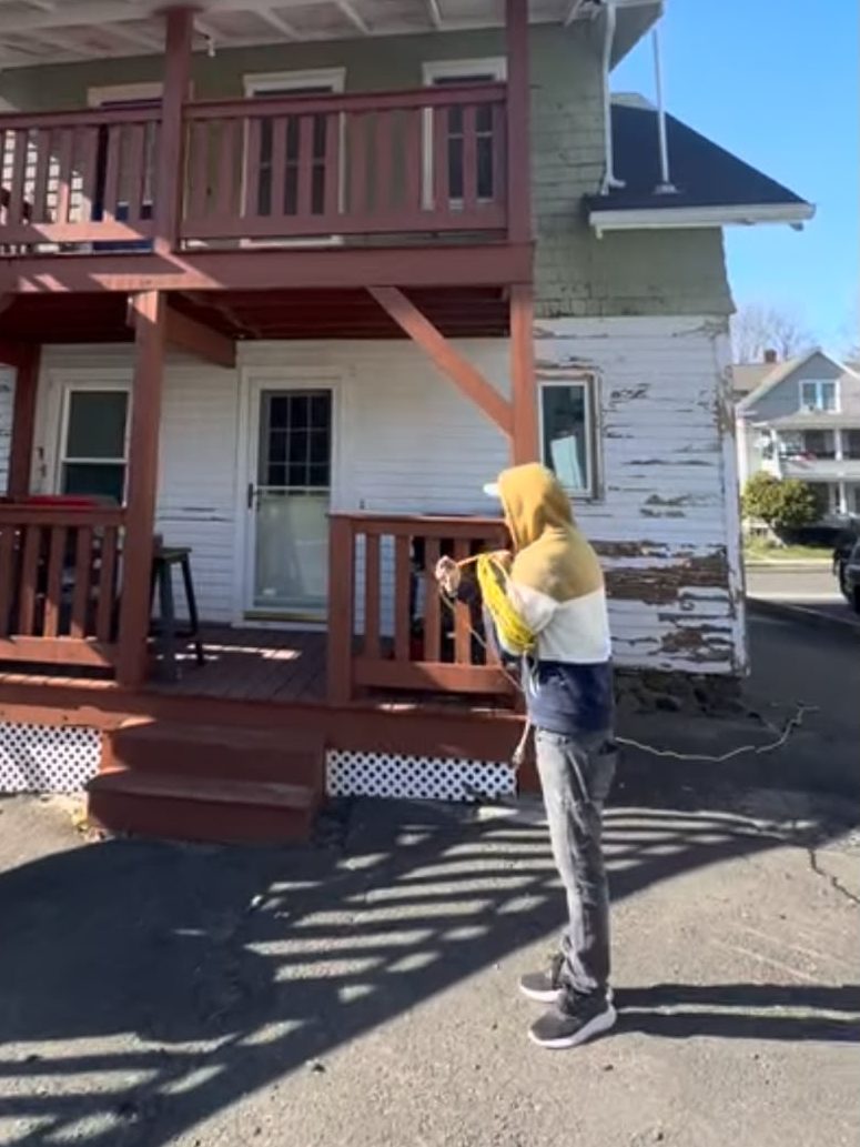 Crew member at work outside a house with peeling white siding and red porches